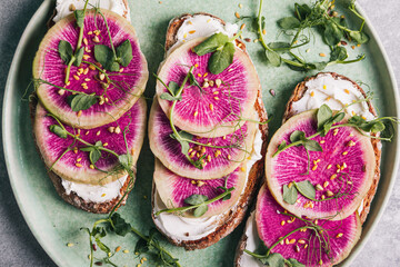 Watermelon radish toast with cream cheese and micro-green peas in a green ceramic plate.