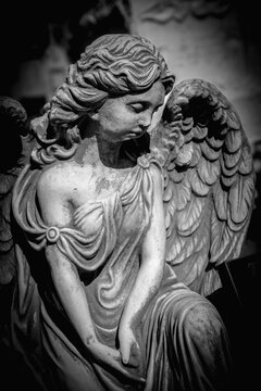 Dramatic photo of sad angel with deep shadows. Fragment of ancient statue. Death and pain concept. Vertical image.