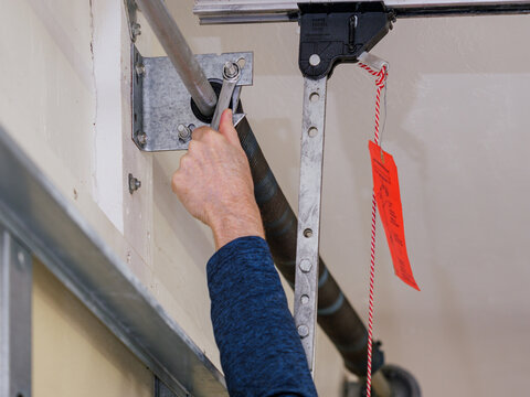 Man repairing electric garage door coiled tension spring. Installing and adjusting overhead garage door opener.