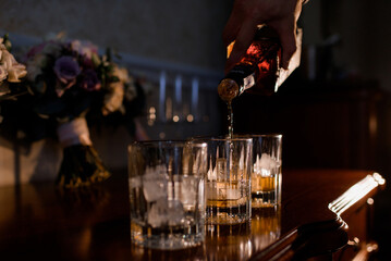 Close up view of man pouring whiskey into glasses. Concept of luxury party.