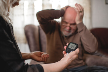 Senior woman checking blood sugar of her diabetic husband at home
