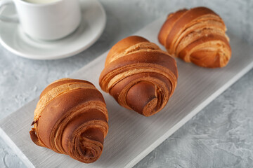 Freshly baked fragrant croissant with a cup of milk on a light background