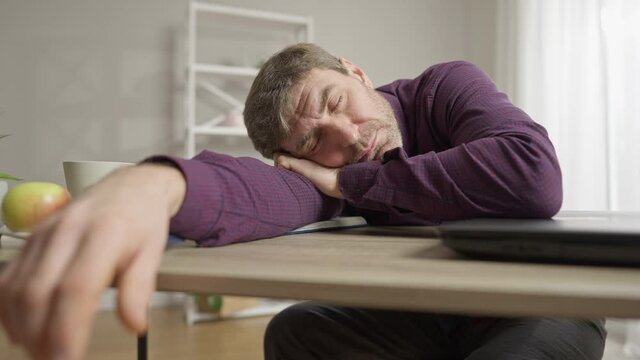 Exhausted middle aged Caucasian man sleeping on table at home. Portrait of overworked handsome guy tired of remote working indoors. New normal on coronavirus lockdown.