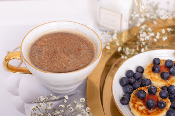 Morning breakfast - coffee and cheesecakes with blueberries, decorated with flowers and candlelight on golden plate