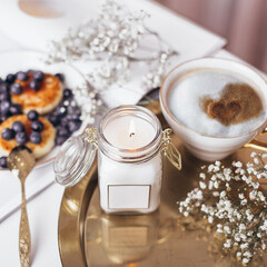Morning breakfast - coffee and cheesecakes with blueberries, decorated with flowers and candlelight on golden plate