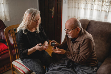 Senior woman checking blood sugar of her diabetic husband at home
