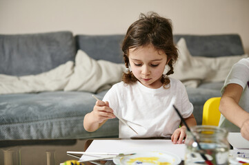 Little girl with braids sitting at table, drawing or painting . Children's creativity concept.