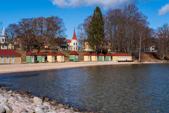 Colorful bath cabins lined up next to sandy beach numbered in roaman numbers with city of Hjo in background, Sweden