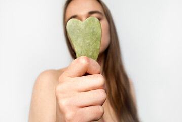 Beautiful girl  with beauty gua sha quartz stone for massage, blonde shows a jade gua sha for the face at the camera. Selective focus.  Cosmetic trend.