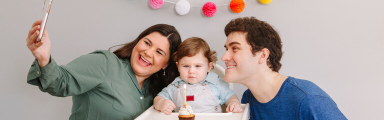 Mother father dad taking selfie photo with child boy. Caucasian family with baby celebrating first birthday. Cupcake dessert with one candle. Happy birthday lifestyle. Web banner header.