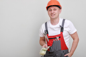 Happy worker in red uniform, protective hard hat holding bundle of dollars, cash money on white background. Male worker for advertisement. labor day