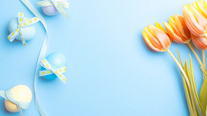 Basket easter decoration: Colourful egg with tape ribbon, spring tulips, white feathers on pastel blue background. Congratulatory easter design. Top view.