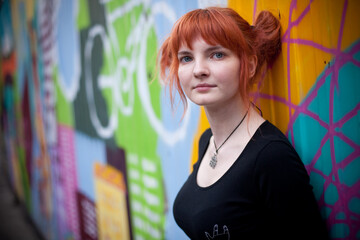 portrait girl with red hair on the background of graphite looks into the camera