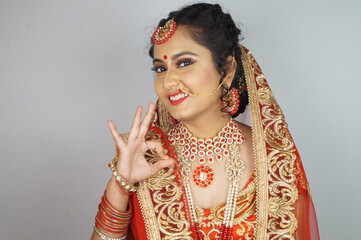 Indian bride with heavy makeup wearing traditional Indian bridal attire and showing OK gesture