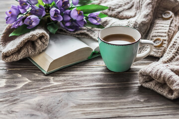 Spring morning coffee. A cup of coffee on a wooden table, an open book and a warm sweater against the background of a bouquet of spring flowers. Still life concept. Cozy morning. 