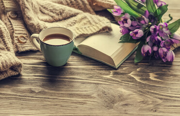 Spring morning coffee. A cup of coffee on a wooden table, an open book and a warm sweater against the background of a bouquet of spring flowers. Still life concept. Cozy morning. 