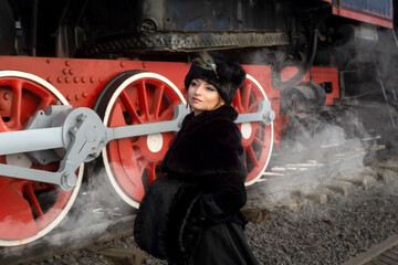Beautiful girl in a historical retro dress on a background of an old steam locomotive, steampunk, at the railway station