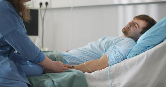Young woman holding hand and consoling male patient while standing by bed during hospital visit