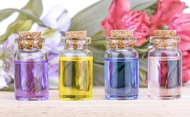 Photo sur Plexiglas Doux monstres Bouteilles colorées en verre huile aromatique et fleurs sur table en bois.