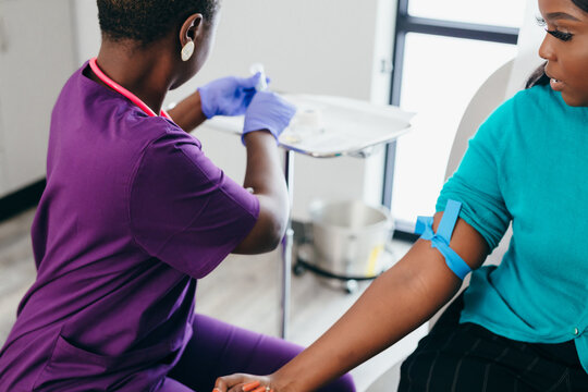 Black nurse collects blood sample from female patient at doctors office