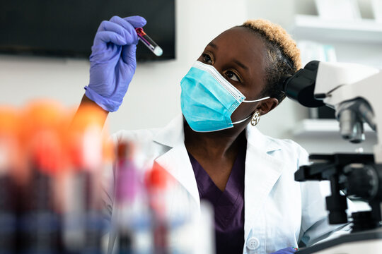 Black female scientist in mask in laboratory with test tubes and microscope equipment