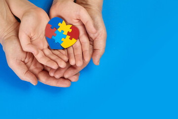 World Autism Awareness day, mental health care concept with puzzle or jigsaw pattern on heart with child and adult hands
