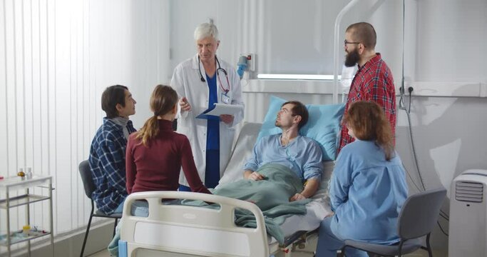 Family and friends visiting patient in hospital ward and talking with doctor.
