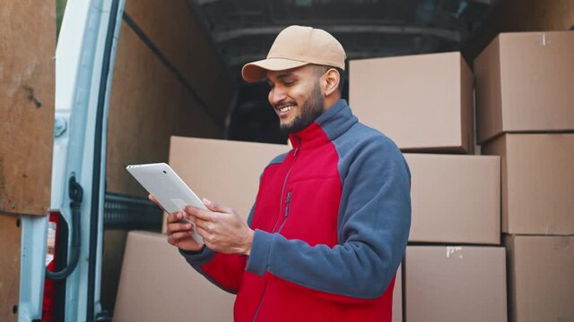 Delivery man using tablet to preview orders. Standing in front of the van with parcels. High quality 4k footage