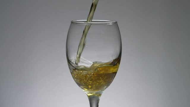 Pouring white wine into a glass. White wine is poured from a bottle into a glass in which splashes. Beautiful slow-motion 4K video of alcohol in a restaurant or at home.