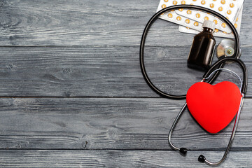 A heart with a stethoscope lies on a wooden background. Healthy heart