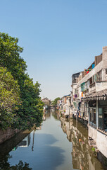 Suzhou China - May 3, 2010: City canal portrait with brown water reflects the backside of houses along the water, and green foliage on other side under blue sky. Laundry adds colors.