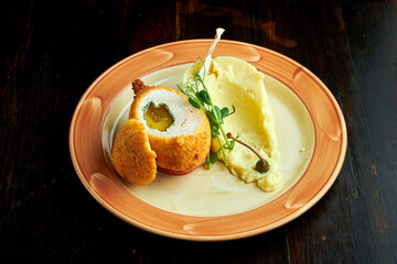 Appetizing Kiev cutlet in breadcrumbs with butter and herbs, served with mashed potatoes in a plate on a dark background. Chicken Kyiv
