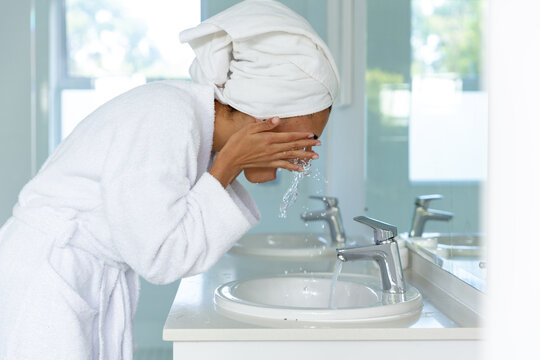 Mixed Race Woman Wearing Bathrobe And Washing Her Face In Bathroom