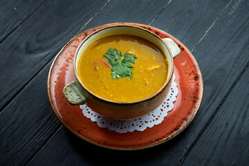 Traditional Moroccan soup - Harira, yellow lentil soup with cilantro in a red plate on a black wood background. Diet soup