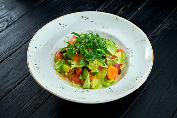Diet and vegetarian salad of mixed vegetables and lettuce with peanut sauce, served in a white plate on a black wood background