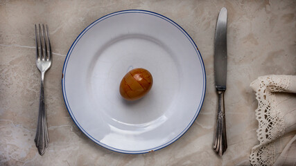 Colored orange egg on a white ceramic plate with silverware cutlery on a marble table. Close up.