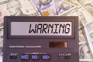 On the table are dollars and a calculator on the electronic board which says WARNING
