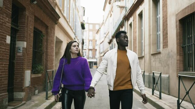 Young millennial interracial couple holding hands walking in street