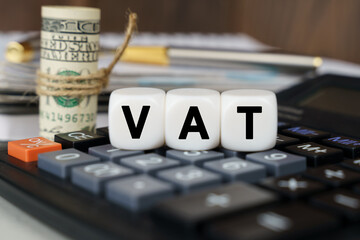There are cubes on the calculator that say - VAT. Nearby out of focus - dollars, notebook and pen