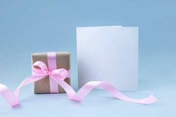 Blank greeting card with small present box with pink ribbon on light blue background
