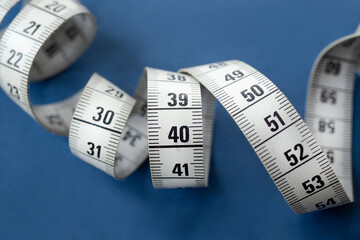 Centimeter tape, fitness and weight loss. Tailor's meter, for sewing, on a blue background. Meter, tape measure, to measure the body, waist in centimeters.