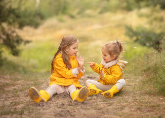 Two children playing in the forest. Happy sisters sitting and smiling in the park.
