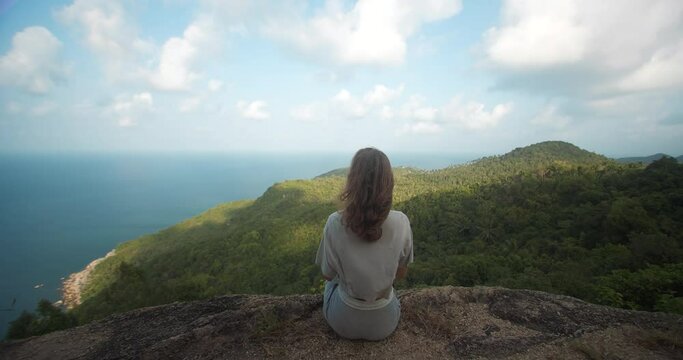 Landscape overview zoom in on  woman from behind sitting on rock cliff and enjoing sea view on the island