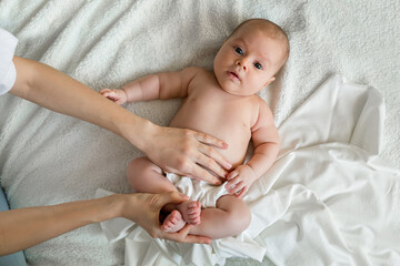 A cute little baby is lying on the bed, mom holds her hand on the baby's tummy. Sick tummy in a newborn , treatment of children under one year old