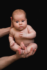 a newborn baby on a black background , an adult holding a baby in his arms