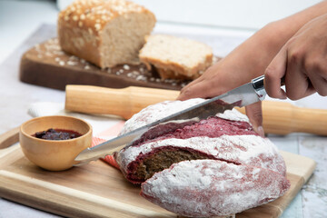 Beautiful hands cutting red velvet bread on wooden surface with blackberry sauce and rolling pin