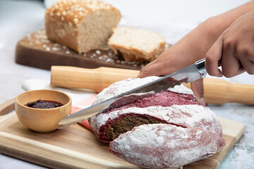 Beautiful hands cutting red velvet bread on wooden surface with blackberry sauce and rolling pin