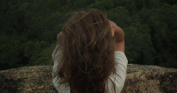 View from above to behing of girl sitting on rock cliff ad overlooking landscape sea view