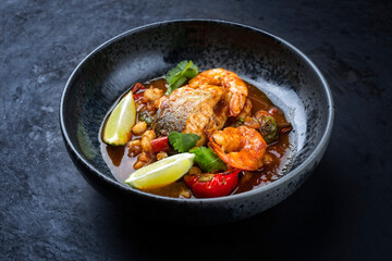 Modern style traditional Mexican seafood pozole soup with fish, king prawns and hominy in a clear sauce served as close-up in design bowl