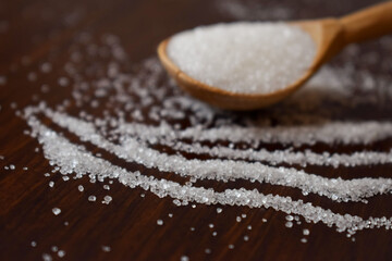 tracks of white sugar crystals.in the background, a blurred wooden spoon with sugar.